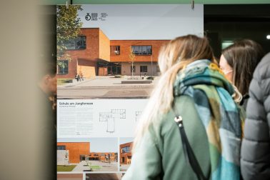Besucher auf der Ausstellung "da! Architektur in und aus Berlin" vor dem Plakat "Grundschule am Jungfernsee" von sehw.