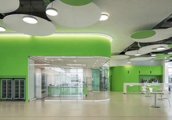 Cafeteria mit grünen Wänden, einer Glastrennwand, runden Deckenelementen und Tischgruppen des IZS, Stuttgart.