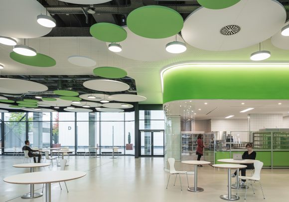 Cafeteria mit grünen Wänden, einer Glastrennwand, runden Deckenelementen und Tischgruppen des IZS, Stuttgart.